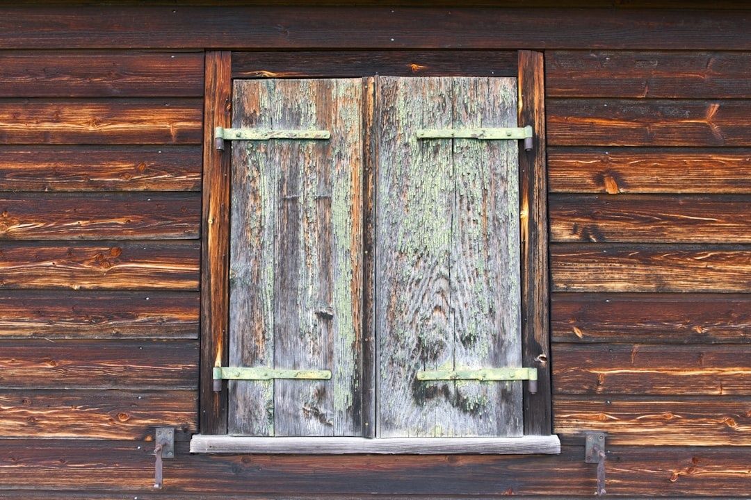 Sliten träfasad med väderbitna, målade fönsterluckor